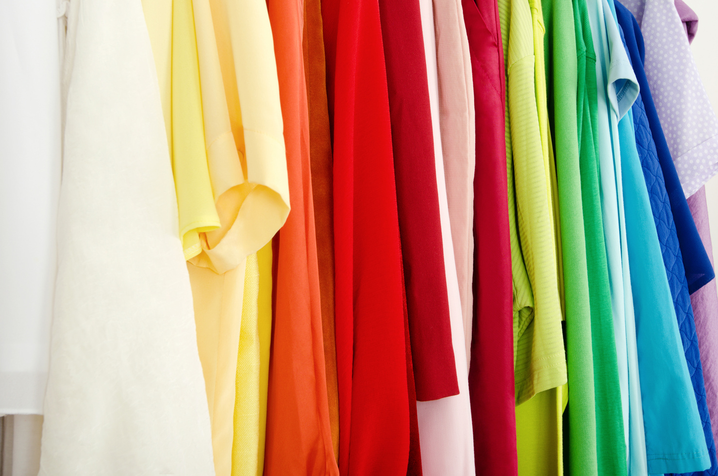 Closeup to color coordinated clothes on hangers in a store.